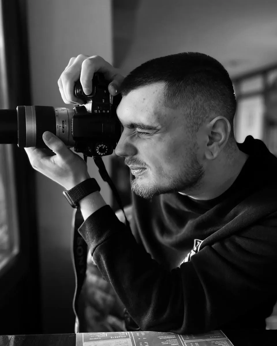 Cosmin Braniște with a camera at a window, black and white